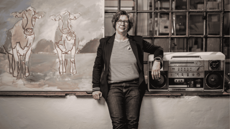 Maren Martschenko steht und sitzt leicht angelehnt an einem Absatz. Neben ihr ein Ghettoblaster und hinter ihr hängt eine Weltkarte.