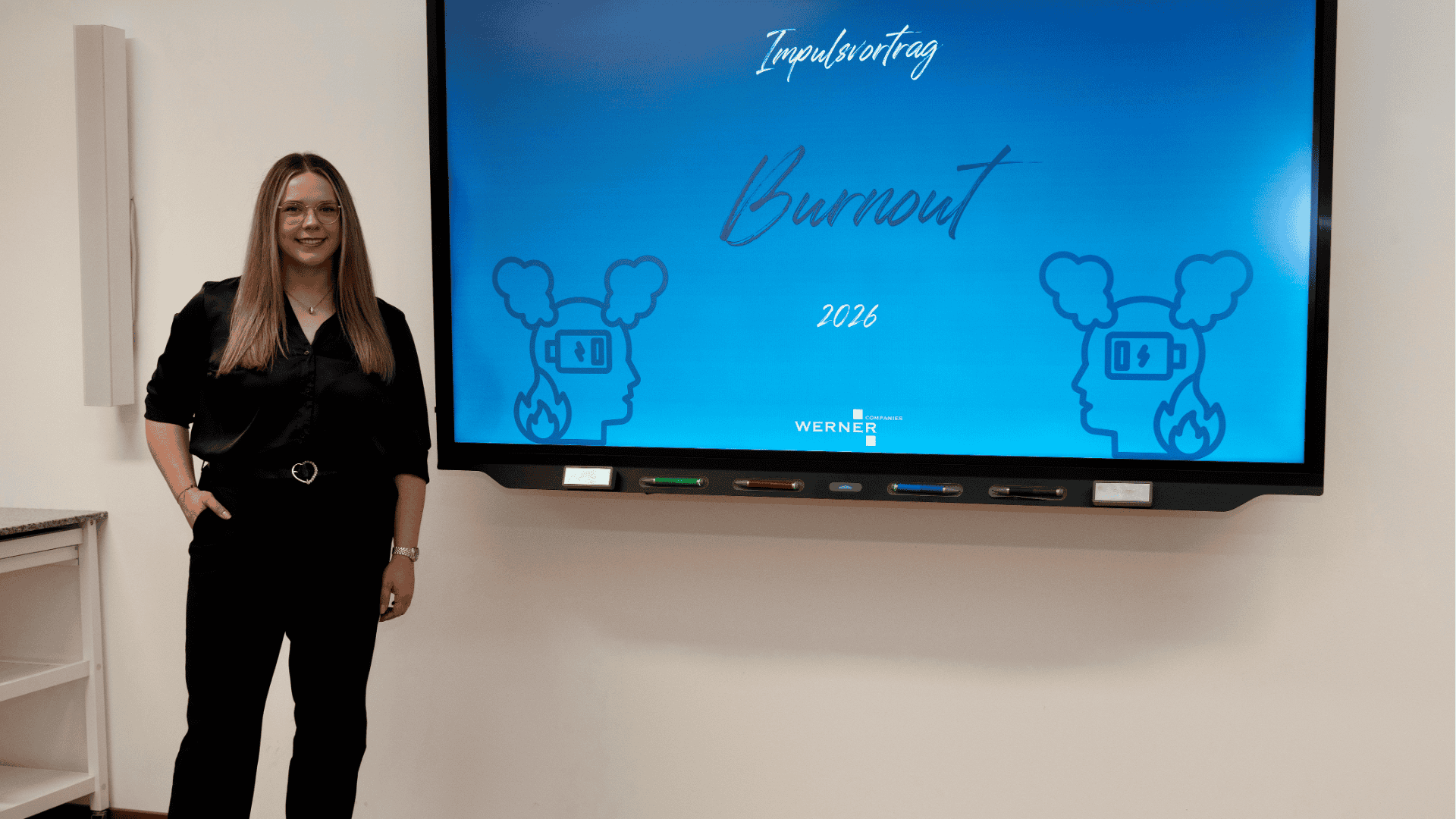 Cindy Papperitz steht der Kamera zugewandt vor einem großen Bildschirm auf dem steht: Impulsvortrag Burnout 2026
