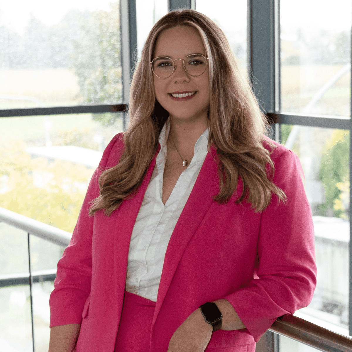 Cindy Papperitz hat einen rosafarbenen Blazer an, steht lässig mit dem linken Ellenbogen angelehnt am Geländer und lächelt in die Kamera. Sie trägt ihr blondes, langes Haar offen.